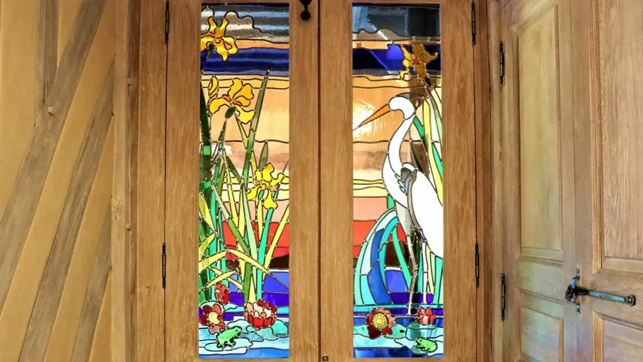 Portes en bois ornées de vitraux représentant des iris, un héron et des nénuphars. L'art de faire des vitraux sublime cette entrée.