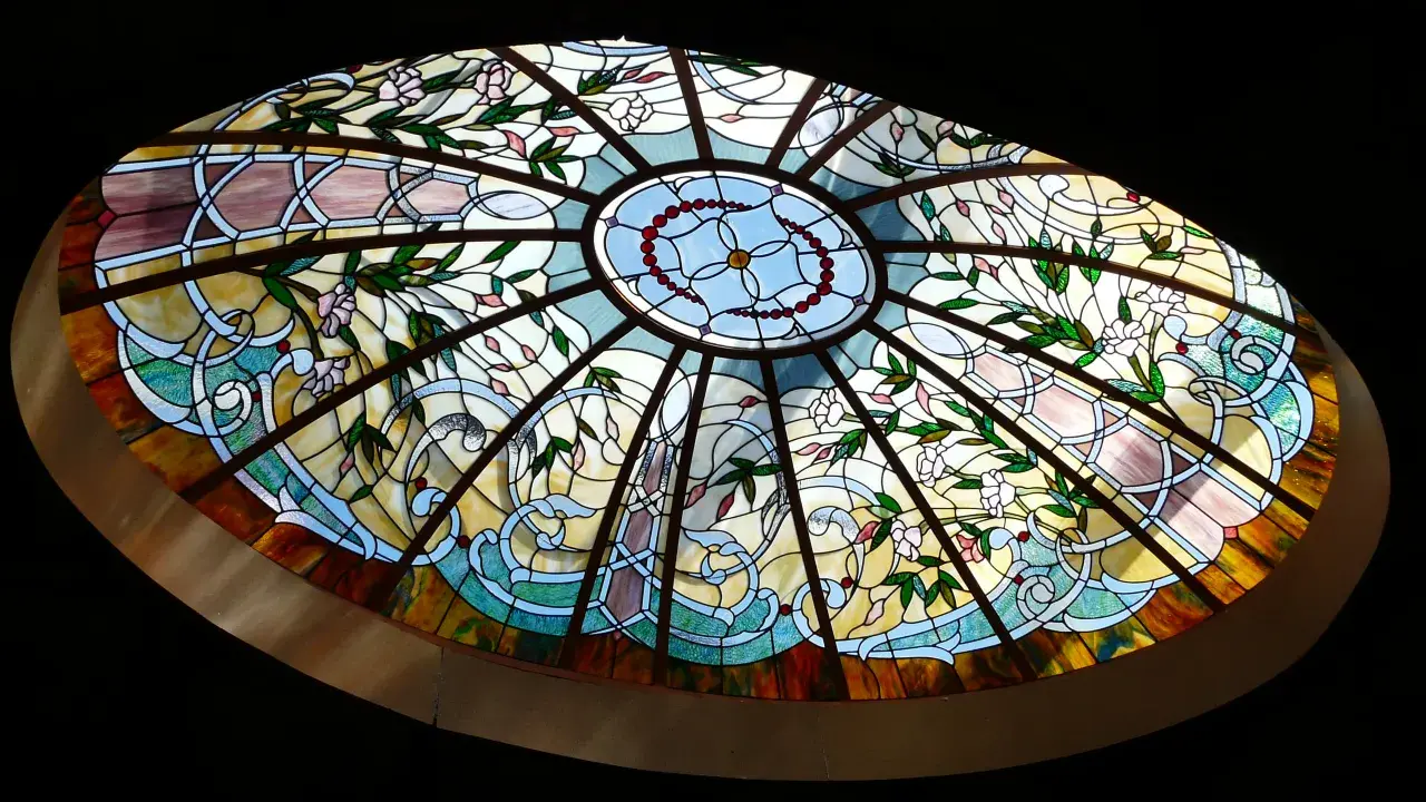 Magnifique vitrail intérieur maison, orné de fleurs roses et de motifs végétaux bleus et jaunes, illuminant la pièce.