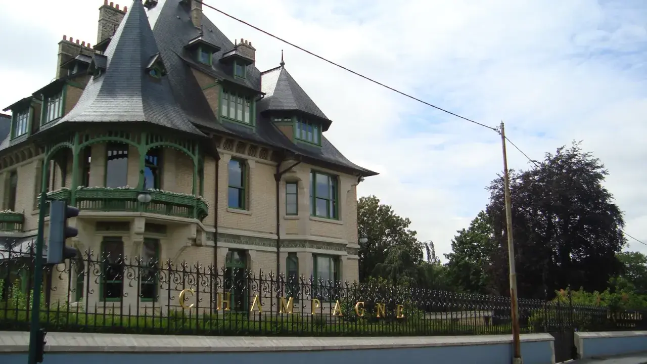 La maison Demoiselle à Reims, une bâtisse de style Belle Époque avec ses toits pointus et sa ferronnerie verte. Le mot "CHAMPAGNE" est visible sur la grille.