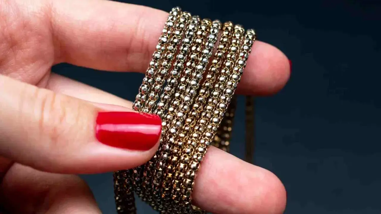 Main d'une femme aux ongles rouges tenant une chaîne de métal doré, montrant comment nettoyer métal doré noirci.