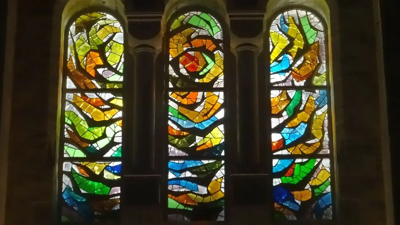 Trois vitraux aux formes abstraites et aux couleurs vives, un exemple de comment éclairer un vitrail pour révéler sa beauté.