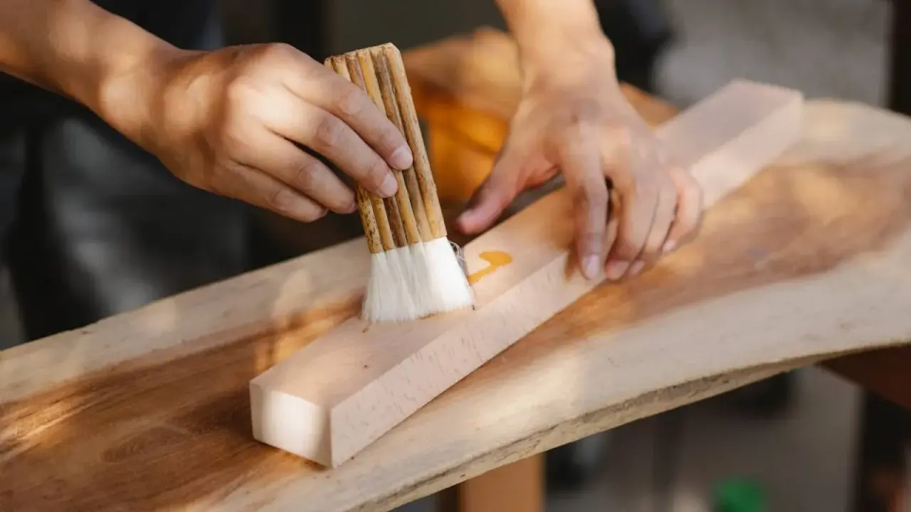 Un artisan ébéniste applique une finition sur un morceau de bois avec un pinceau.