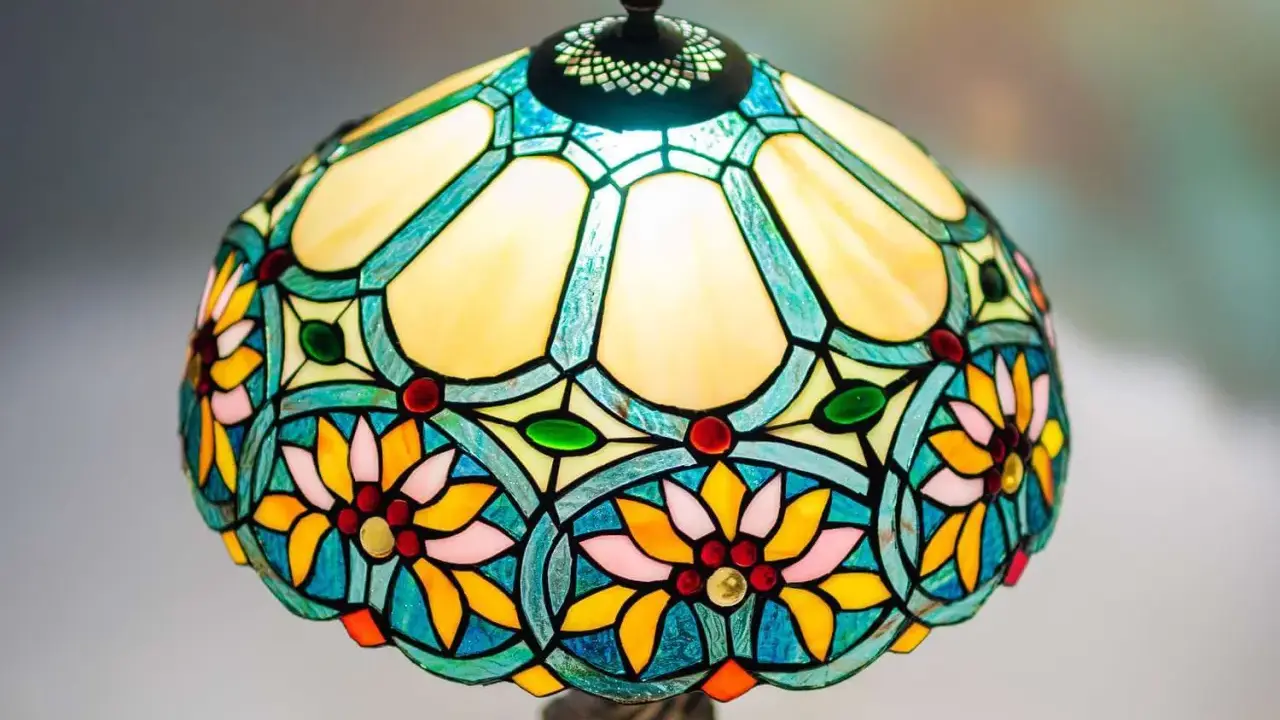 Lampe vitrail aux motifs floraux colorés, avec des pétales jaunes, roses et bleus, et des cabochons rouges et verts.