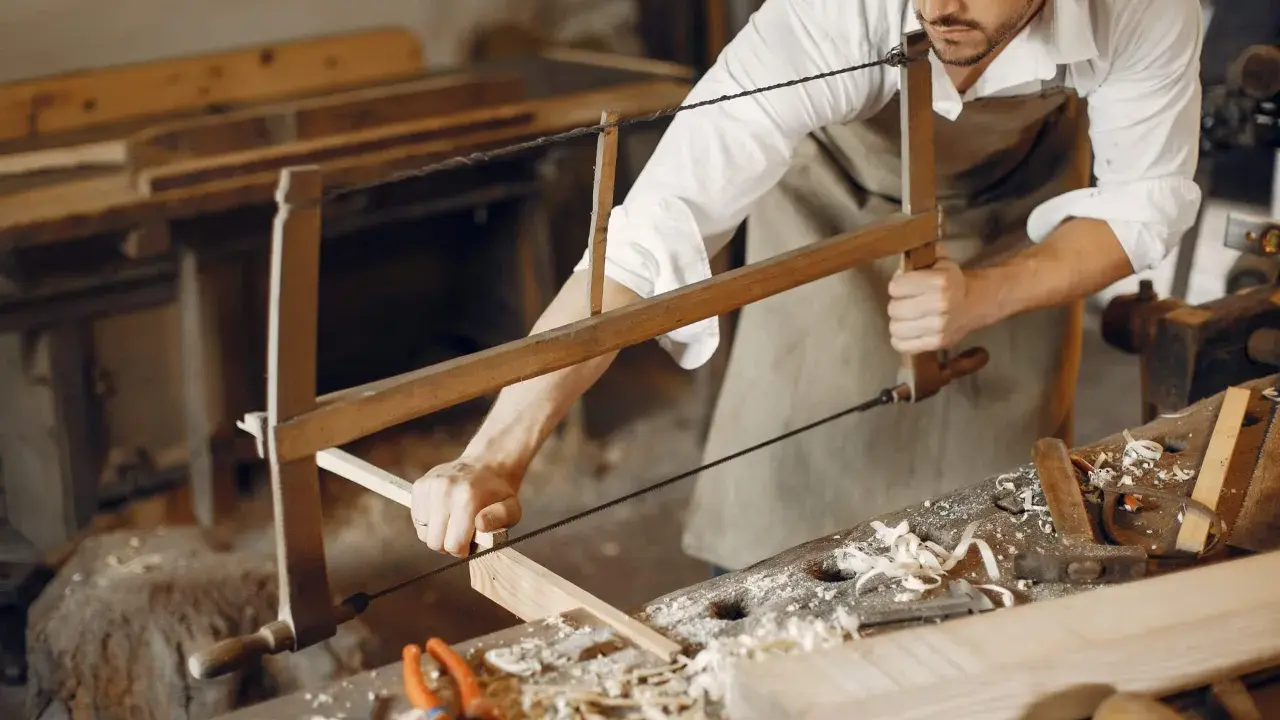 Artisan menuisier travaillant le bois avec une scie, dans un atelier d'ébénisterie d'art.