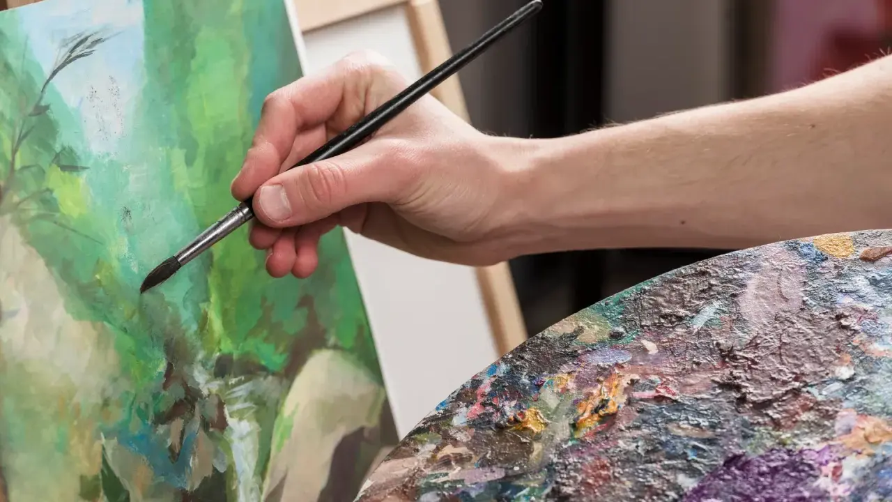 Main d'artiste appliquant la peinture sur une toile, palette colorée à proximité. Une belle technique de peinture en cours.
