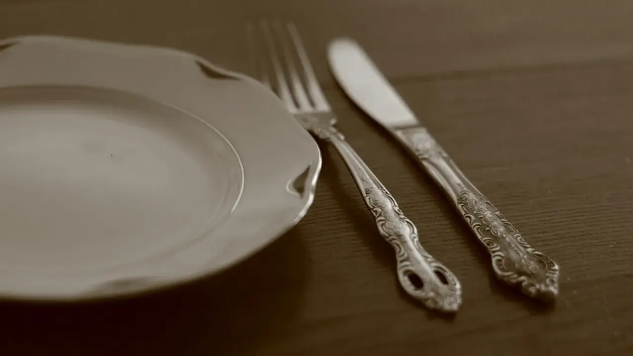 Une assiette blanche et des couverts en métal argenté, prêts pour un repas. L'art de nettoyer des couverts en métal argenté pour qu'ils brillent.