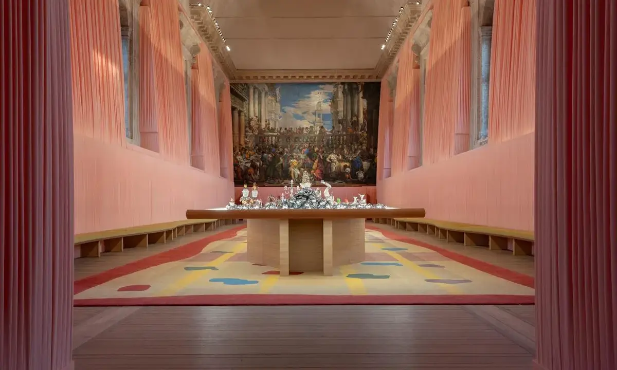 Installation d'art contemporain à Venise, évoquant le *homo faber*. Un tapis coloré et une table ornée de sculptures sous un grand tableau.