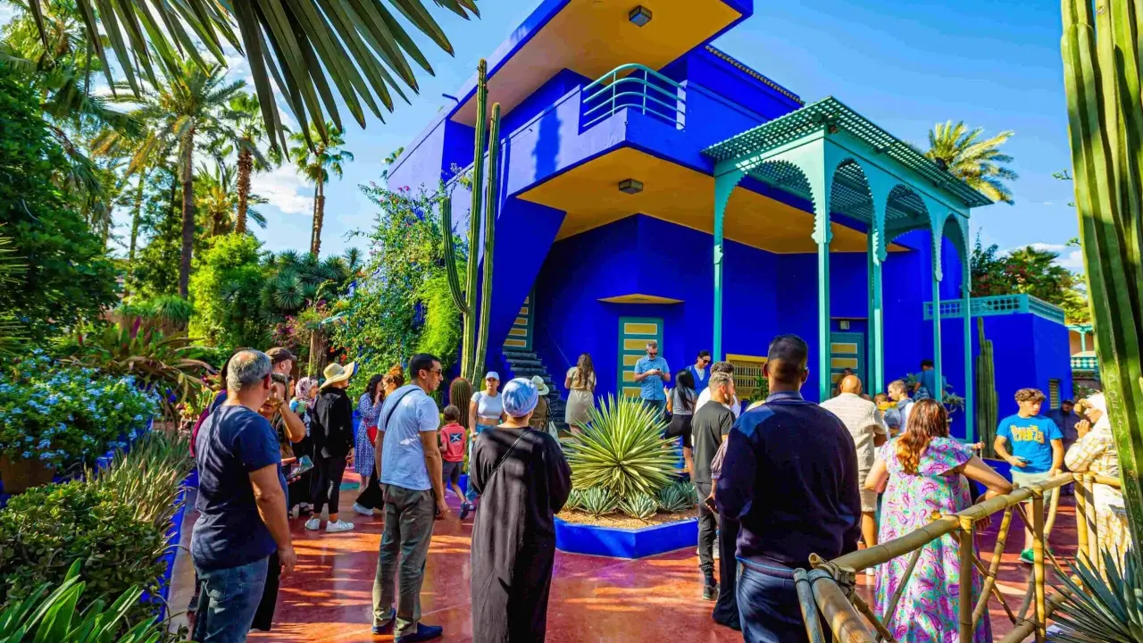 Visiteurs admirant l'architecture vibrante et la végétation luxuriante du jardin Majorelle, un havre de paix bleu cobalt et jaune.