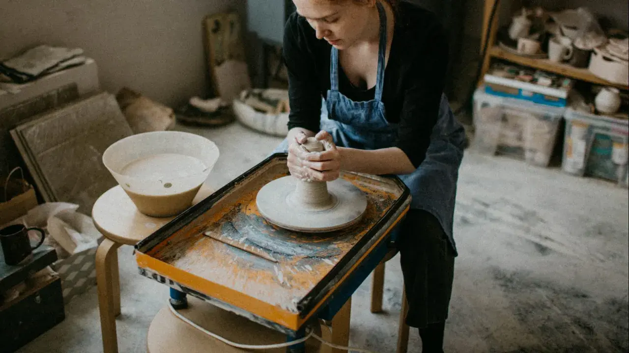 Jeune femme concentrée sur son apprentissage de l'artisanat de la poterie, façonnant l'argile sur un tour.