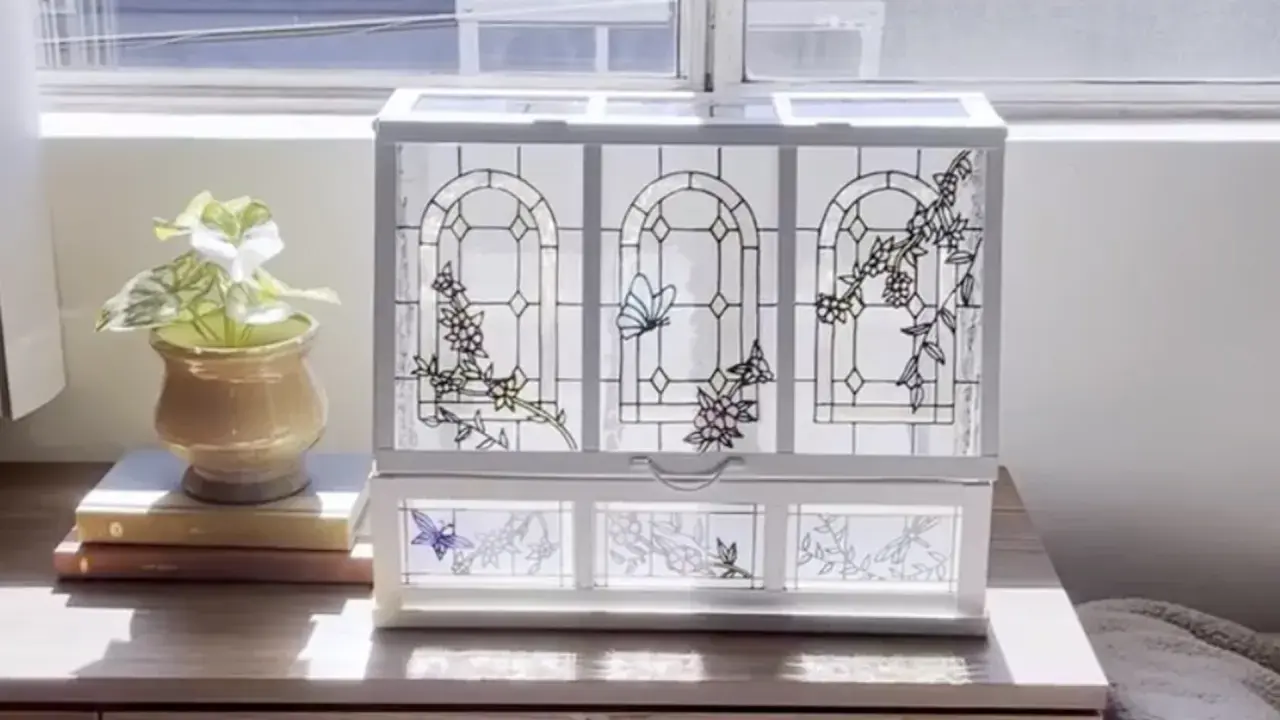 Boîte à bijoux ornée de vitraux décoratifs représentant des papillons et des fleurs, posée sur une commode en bois.