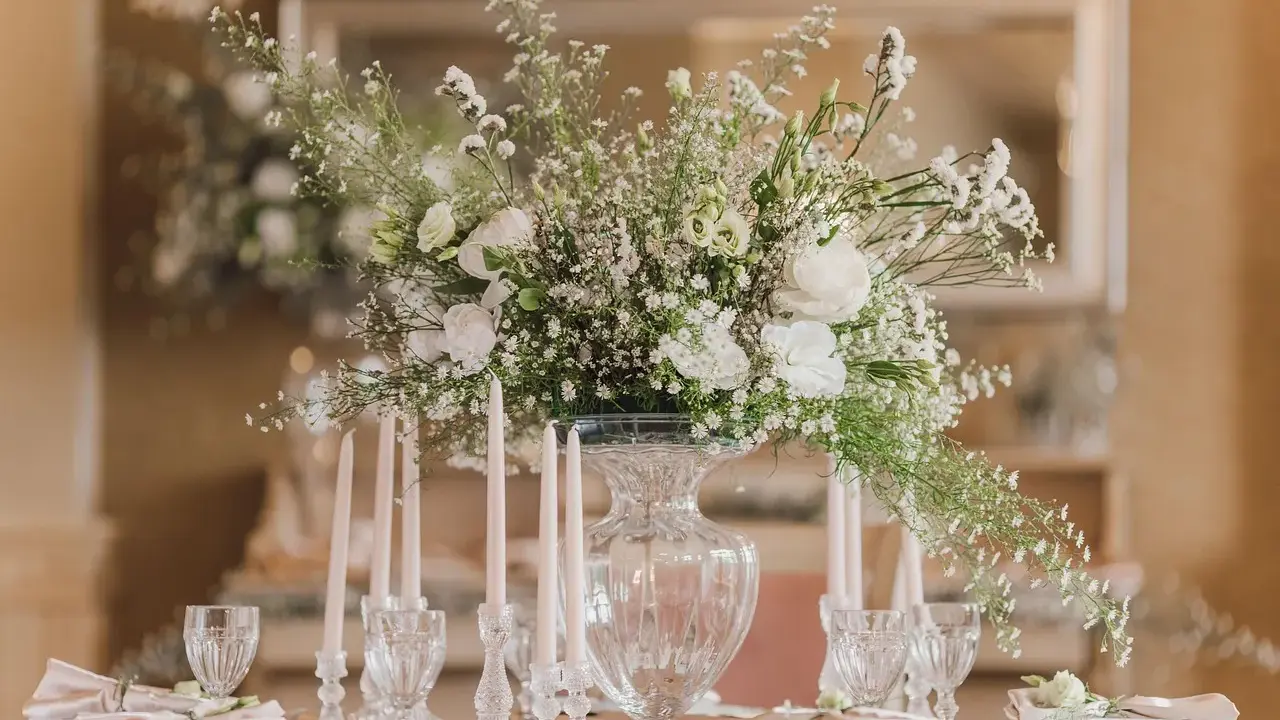 Un bouquet de vitrail fleur, blanc et aérien, orne une table dressée avec des bougies et des verres délicats.