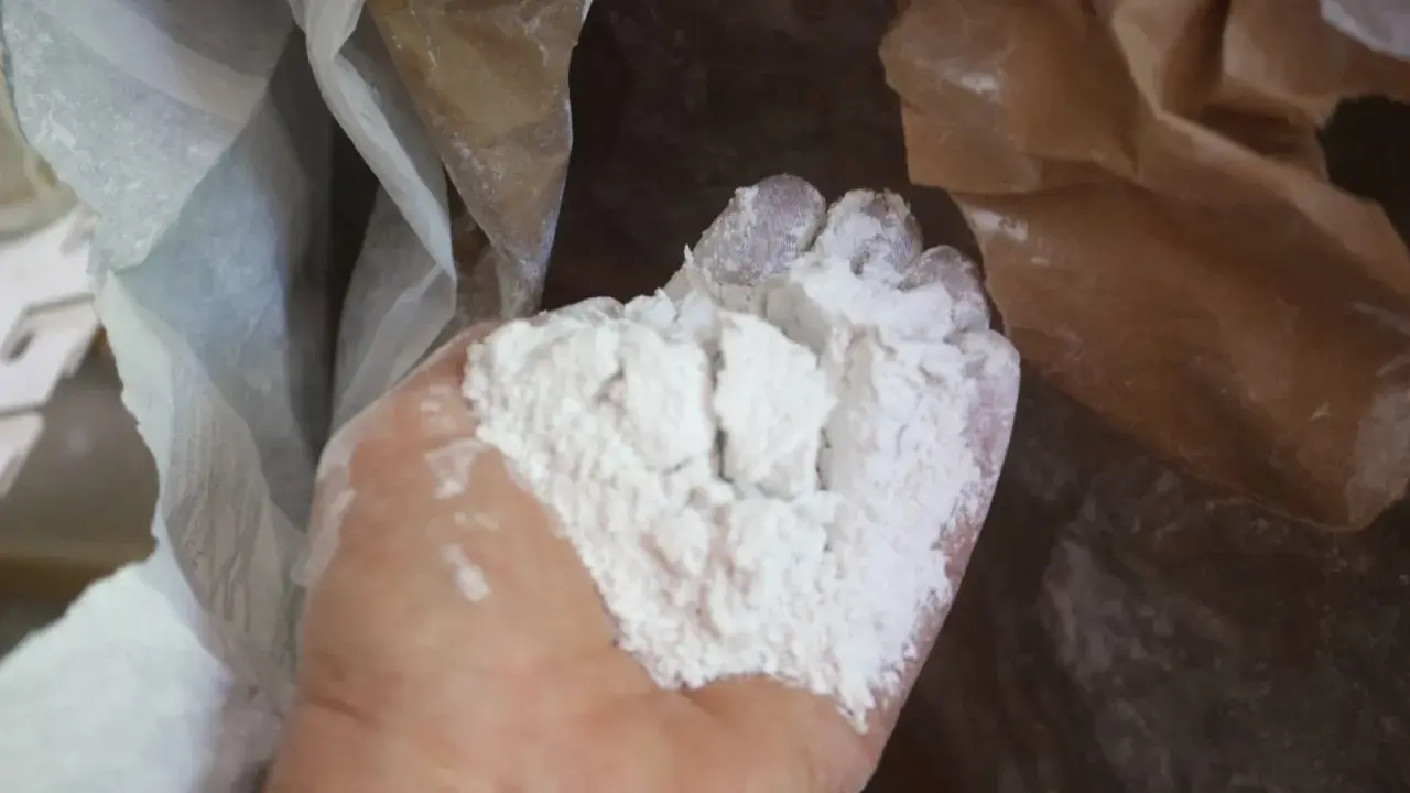 Main d'une personne tenant une poudre blanche fine, de la chaux morte, sortant d'un sac en papier.