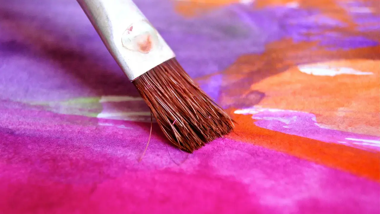 Pinceau humide sur une toile aux couleurs vives, mélangeant le pastel sec et l'eau pour créer des dégradés vibrants de rose, violet et orange.