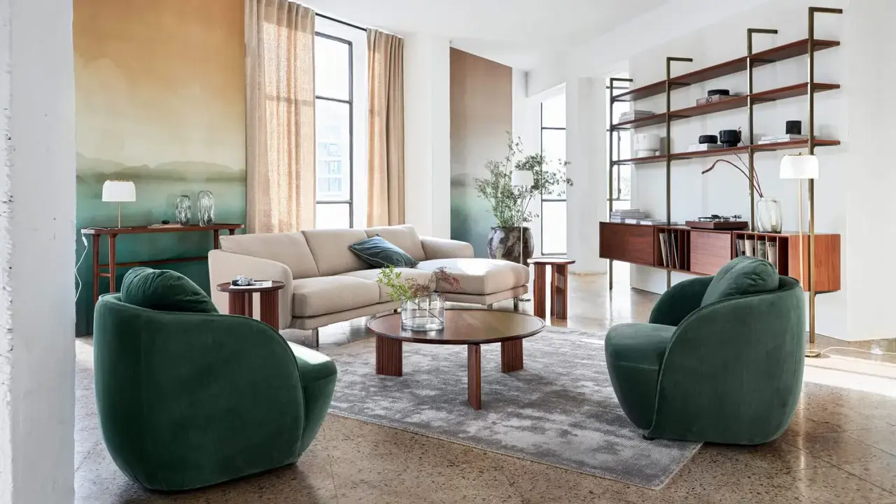 Salon au style mid century avec canapé beige, fauteuils verts velours, table basse ronde en bois et étagères murales.