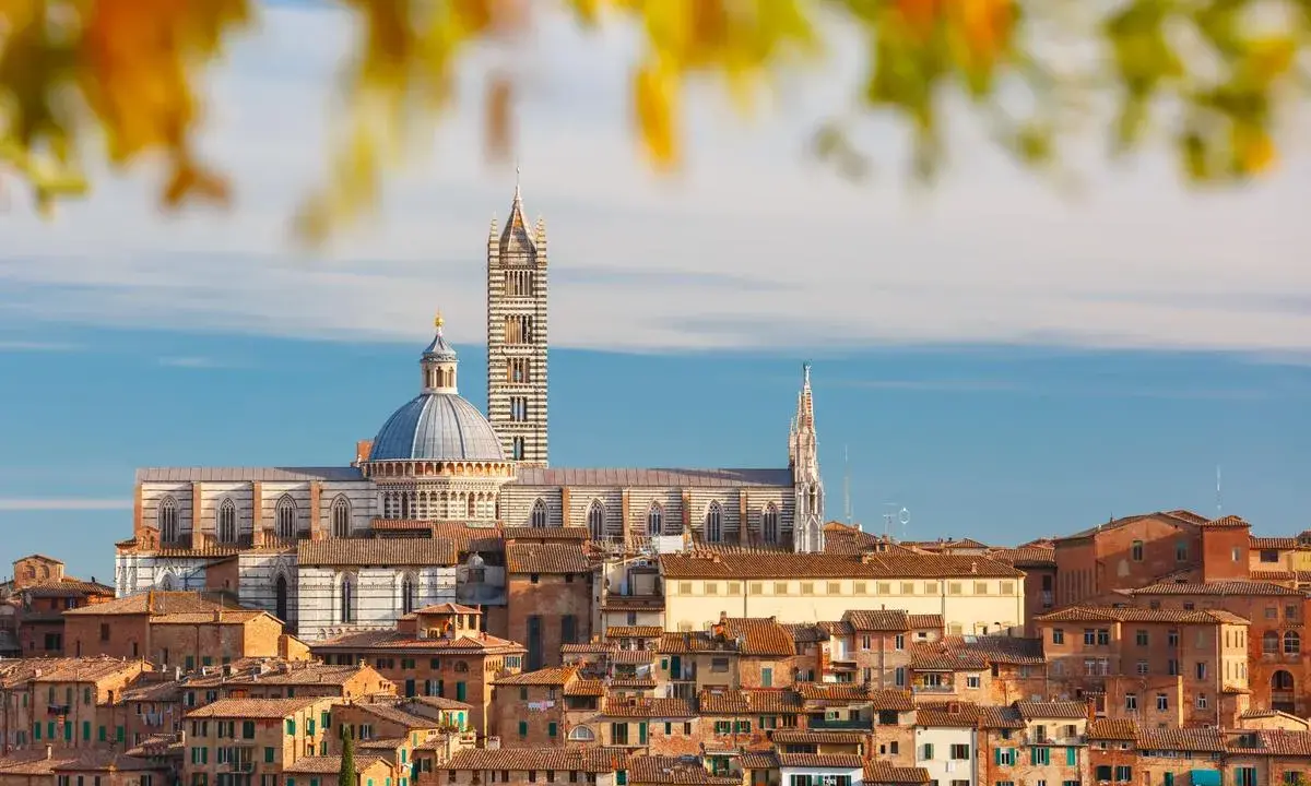Vue panoramique de la ville de Sienne, avec sa cathédrale imposante et ses toits de tuiles ocres, baignée par la lumière dorée de la terre de sienne.