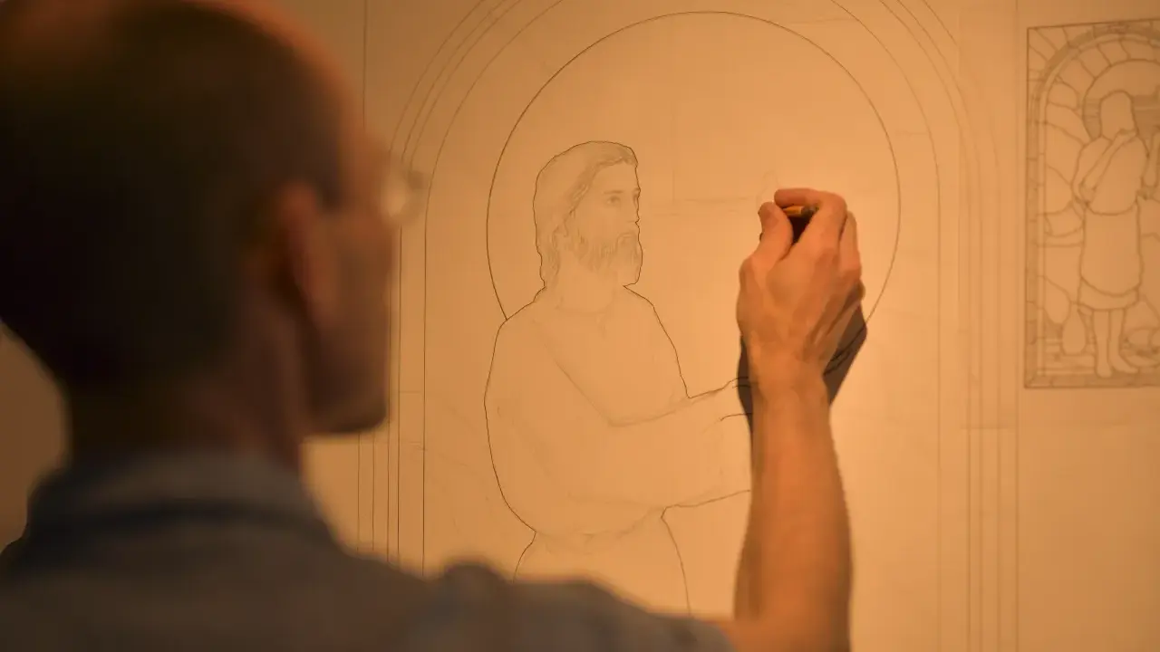 Un artiste esquisse un dessin vitraux, le visage de Jésus prenant forme sous son crayon.
