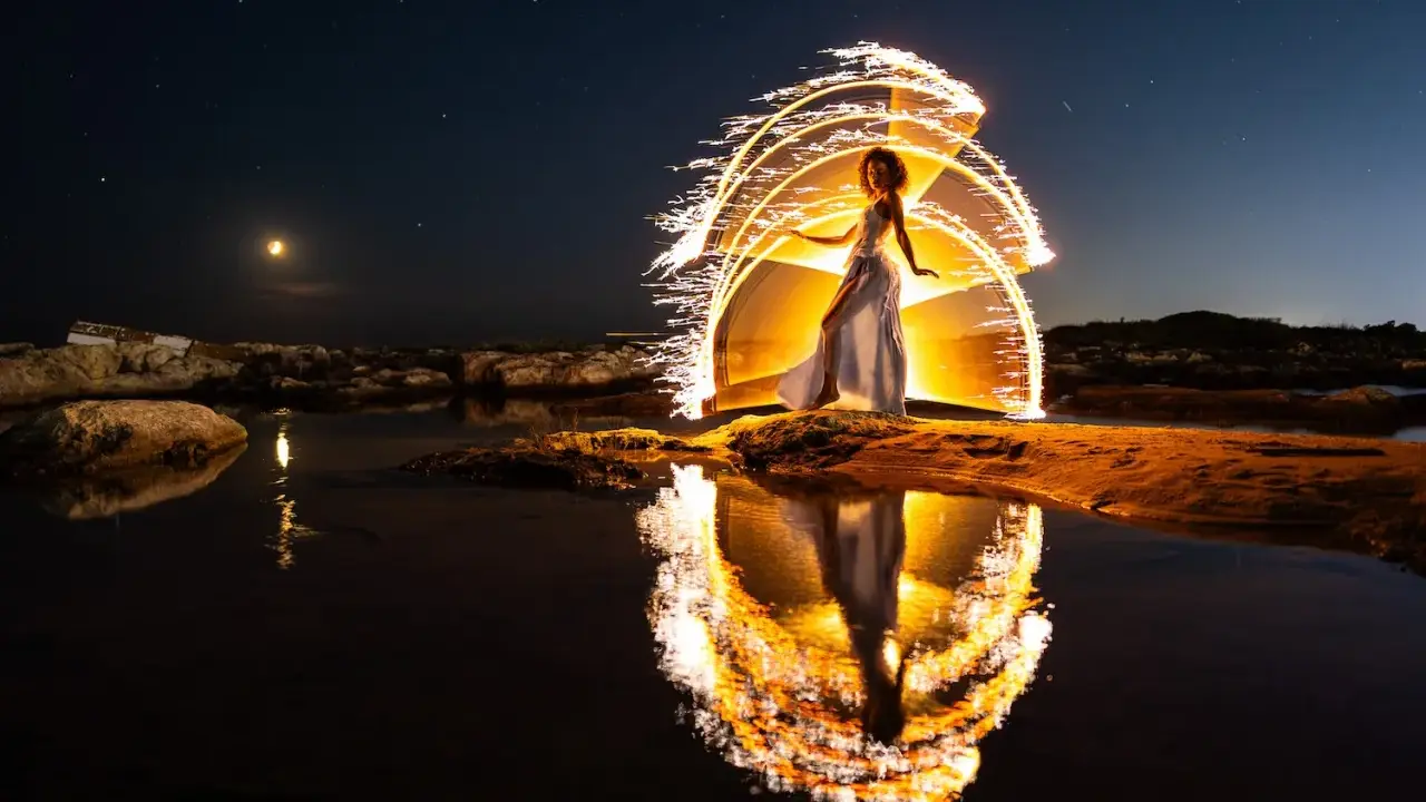 Une femme en robe blanche danse sous un ciel étoilé, entourée d'un halo de lumière incandescente, comme un **verre soleil** reflété dans l'eau.