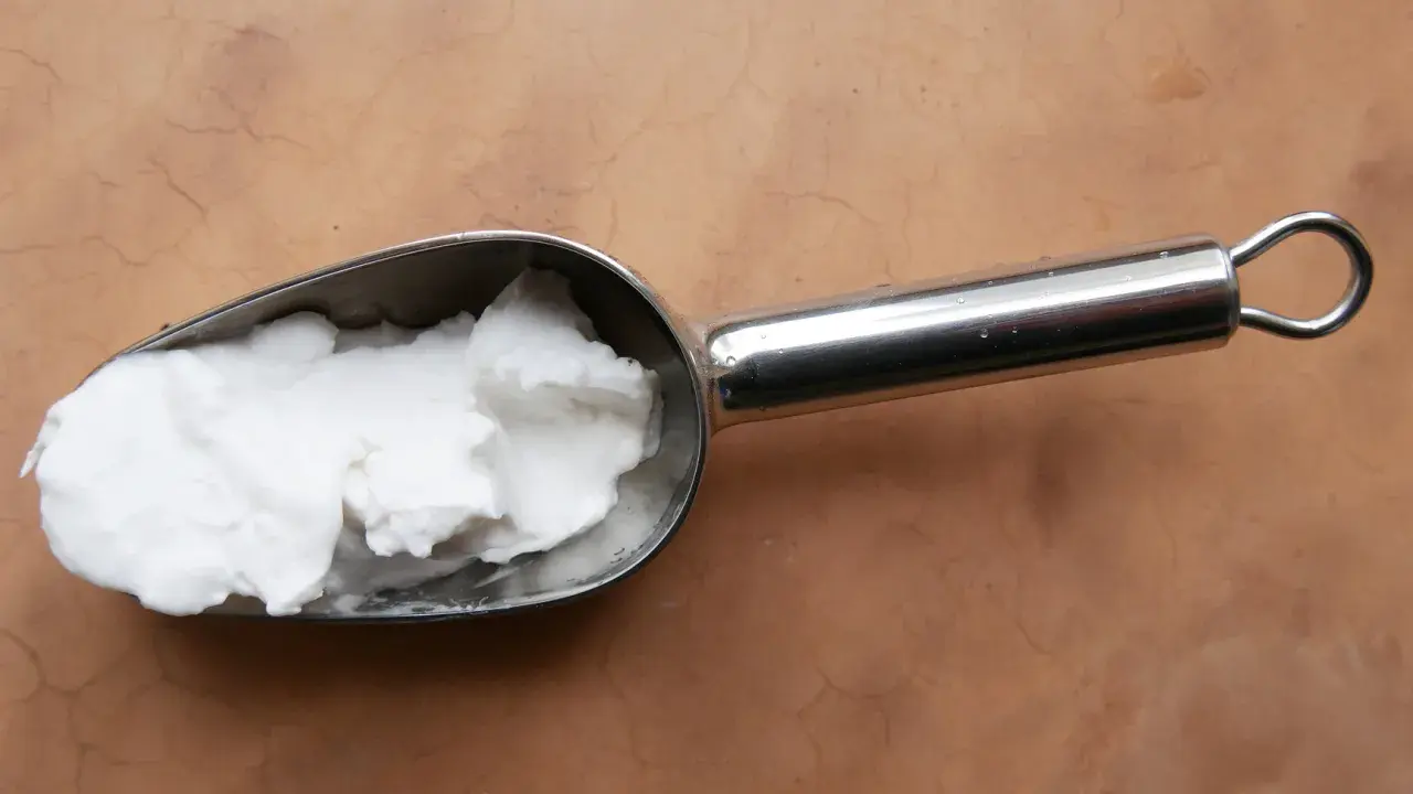 Une cuillère métallique contient une pâte blanche, peut-être de la cire saponifiée sur enduit chaux, prête à être appliquée.