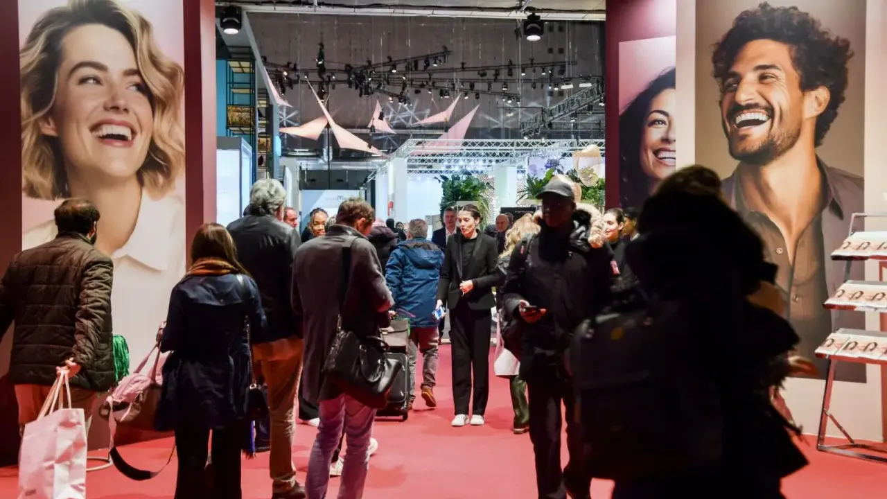 Foule dans un salon, devant de grandes affiches publicitaires. L'esprit meuble est palpable, les gens déambulent, curieux.