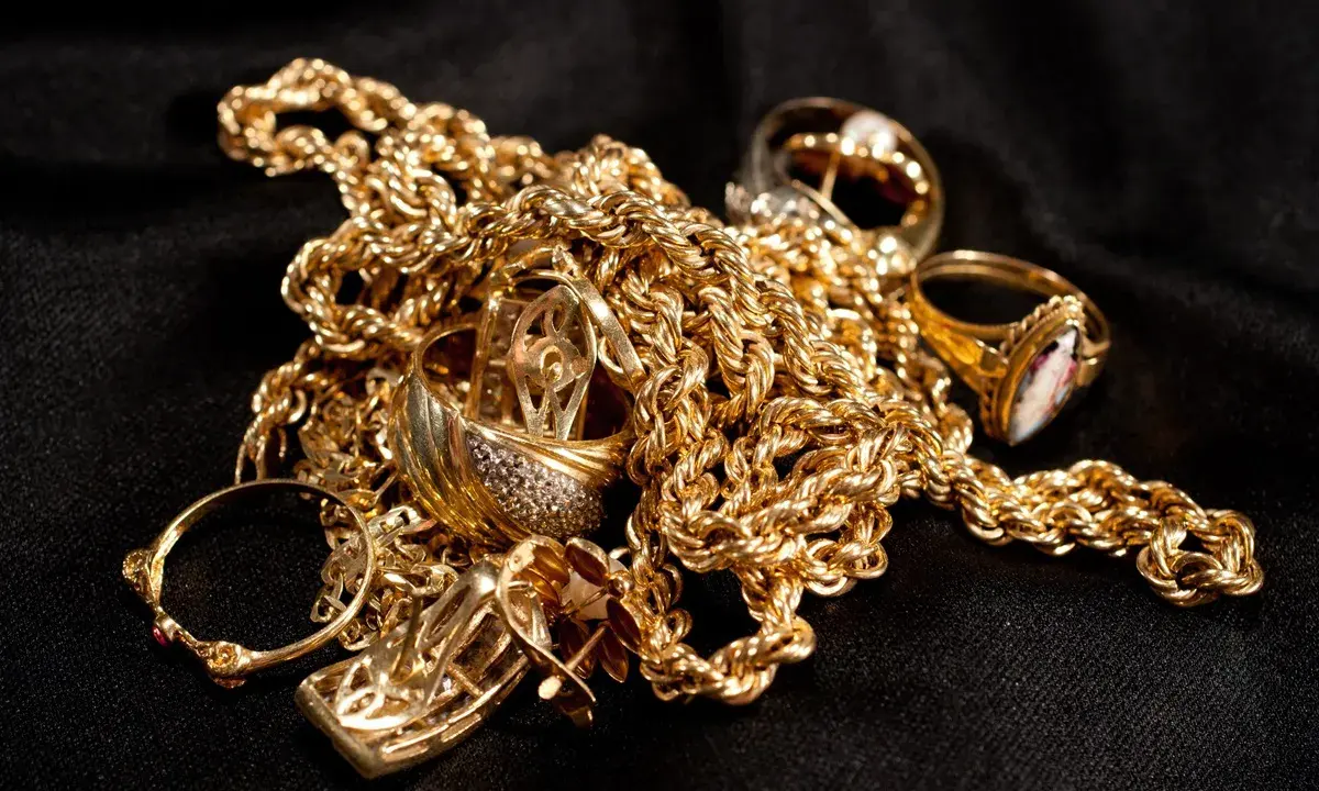 Un amas de bijoux en or, chaînes et bagues, sur fond noir. Pour savoir comment reconnaître de l'or sur une pierre, observez sa couleur et son éclat.
