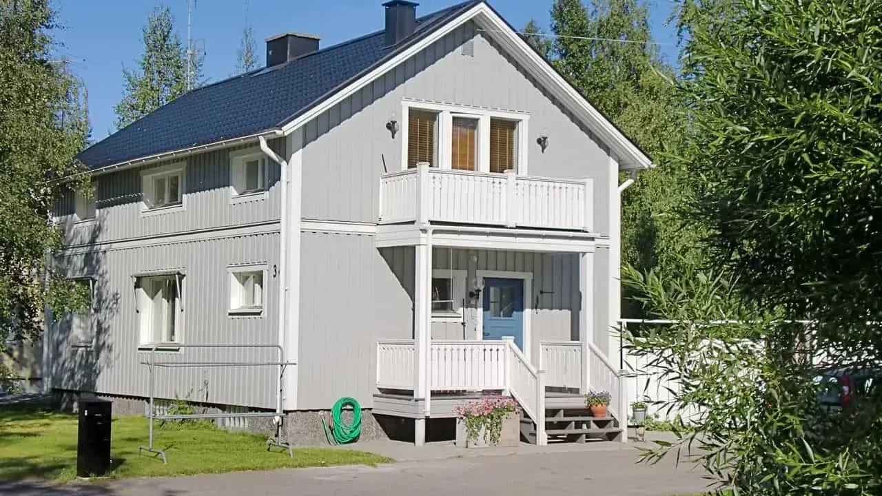 Maison à deux étages avec une peinture suédoise blanche, un balcon, une porte bleue et un jardin verdoyant.