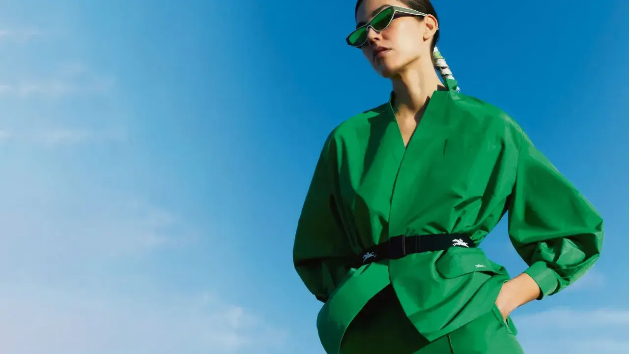 Une femme en tenue verte éclatante, lunettes de soleil futuristes, pose sous un ciel bleu. Un **cahier de tendance** inspirant.