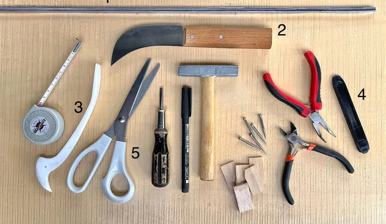 Outils pour le **matériel vitrail** : ruban à mesurer, ciseaux, couteau, marteau, pinces, clous et petits morceaux de bois.
