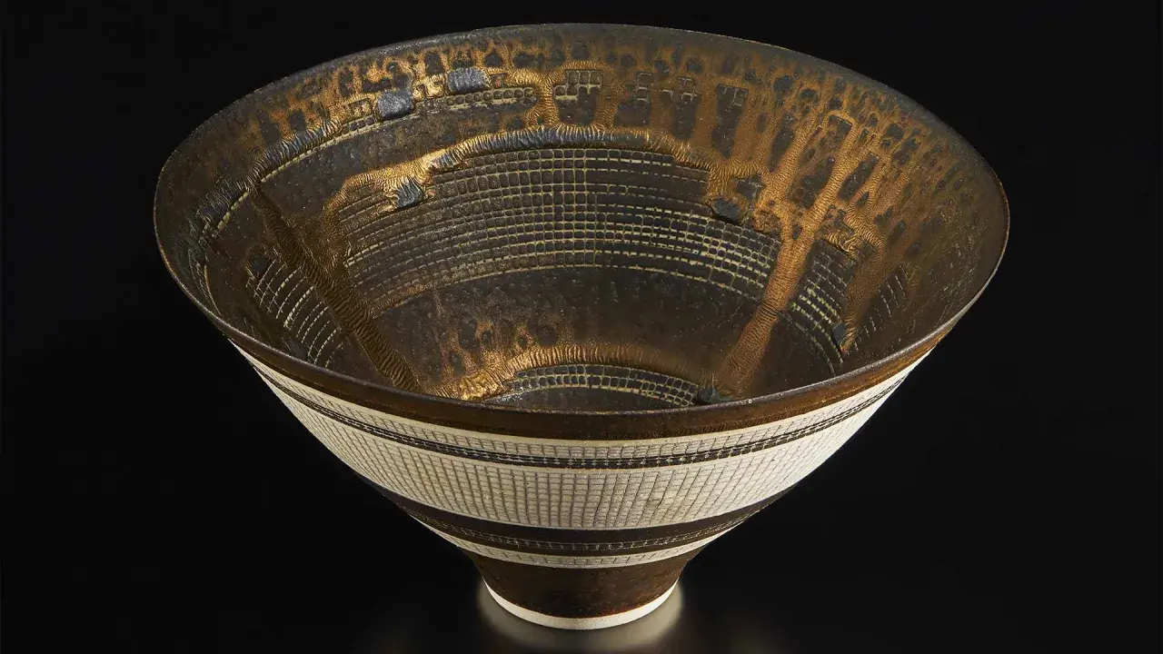 Vase texturé aux reflets dorés et noirs, œuvre d'un céramiste connu, évoquant une cité futuriste.