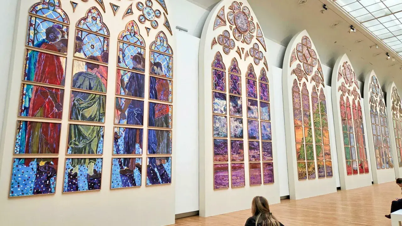 Des vitraux contemporains de Notre-Dame, des œuvres vibrantes composées de multiples panneaux peints, évoquant des scènes humaines et des paysages colorés.