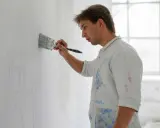Un peintre applique une couche de chaux éteinte sur un mur, esquissant un portrait.
