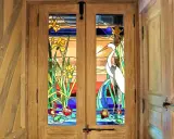 Portes en bois ornées de vitraux représentant des iris, un héron et des nénuphars. L'art de faire des vitraux sublime cette entrée.