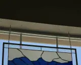 Comment fixer un vitrail sur une fenêtre : un panneau de verre bleu et blanc est suspendu par des chaînes à des crochets fixés au plafond.