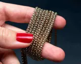 Main d'une femme aux ongles rouges tenant une chaîne de métal doré, montrant comment nettoyer métal doré noirci.