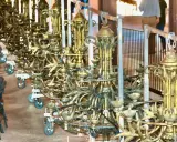 Une rangée de grands candélabres dorés, prêts pour un événement. Ce lustrier métier, complexe et orné, attend d'illuminer la scène.