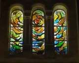 Trois vitraux aux formes abstraites et aux couleurs vives, un exemple de comment éclairer un vitrail pour révéler sa beauté.