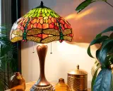 Lampe tiffany origine, abat-jour en vitrail coloré avec libellules, sur une table en bois avec des plantes.