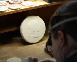 Un graveur métier travaille sur un moule en plâtre orné d'un profil antique. D'autres médailles sont visibles sur l'établi.