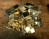 Des petits carrés de laiton brillants, prêts pour un projet de comment décaper du laiton. Ils sont dans des sacs en plastique sur une table en bois.