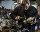Un orfèvre au travail, martelant délicatement un vase en métal dans son atelier rempli d'outils.