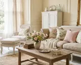 Un salon cosy et lumineux, ambiance intérieur shabby chic. Canapé beige, fauteuils, coussins fleuris et un bouquet de roses.