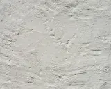 Texture d'enduit à la chaux blanc, présentant des irrégularités et des taches subtiles, témoignant de son application manuelle.