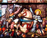 Vitrail de Jeanne d'Arc, la Pucelle d'Orléans, en armure sur son cheval blanc, brandissant son épée au milieu d'une bataille.