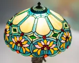 Lampe vitrail aux motifs floraux colorés, avec des pétales jaunes, roses et bleus, et des cabochons rouges et verts.