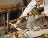 Artisan menuisier travaillant le bois avec une scie, dans un atelier d'ébénisterie d'art.
