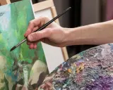 Main d'artiste appliquant la peinture sur une toile, palette colorée à proximité. Une belle technique de peinture en cours.