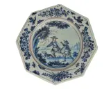 Assiette octogonale en céramique de Marseille, décorée de deux hommes et d'un chien dans un paysage champêtre, bordée de motifs floraux bleus.