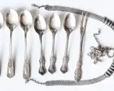 Six cuillères et une fourchette anciennes, ornées, sont disposées avec une chaîne argentée. Idéal pour apprendre comment nettoyer l'argenterie.