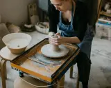 Jeune femme concentrée sur son apprentissage de l'artisanat de la poterie, façonnant l'argile sur un tour.