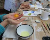Préparation d'une tempera peinture à l'oeuf : un jaune d'œuf est tenu dans une main au-dessus d'un bol contenant le blanc.