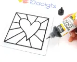 Main noire pour un modèle vitrail en forme de cœur. Un tube de peinture contour est tenu par une main.